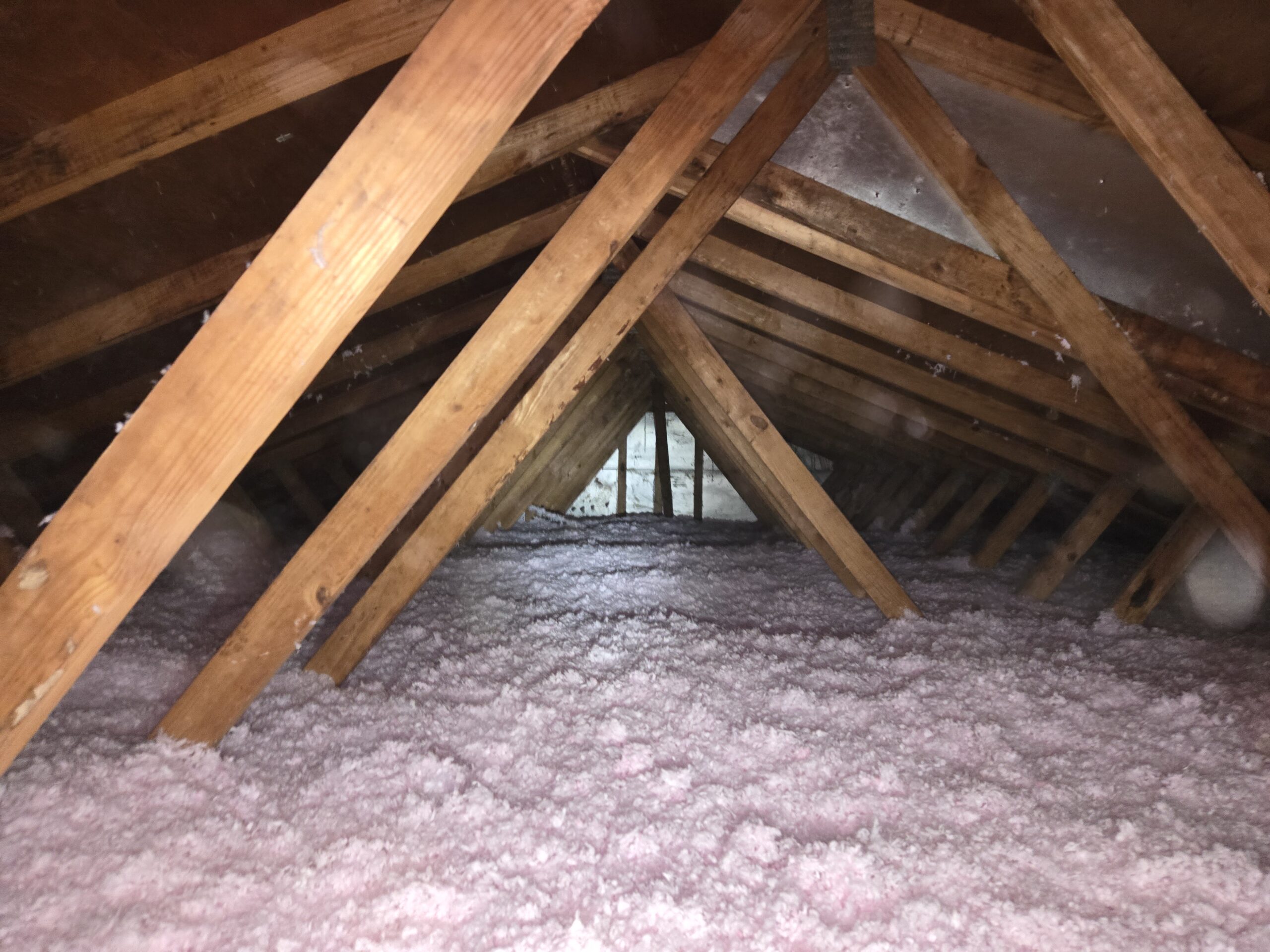 Existing pink blown-in fiberglass insulation covering the attic floor of a Pasadena, Maryland home