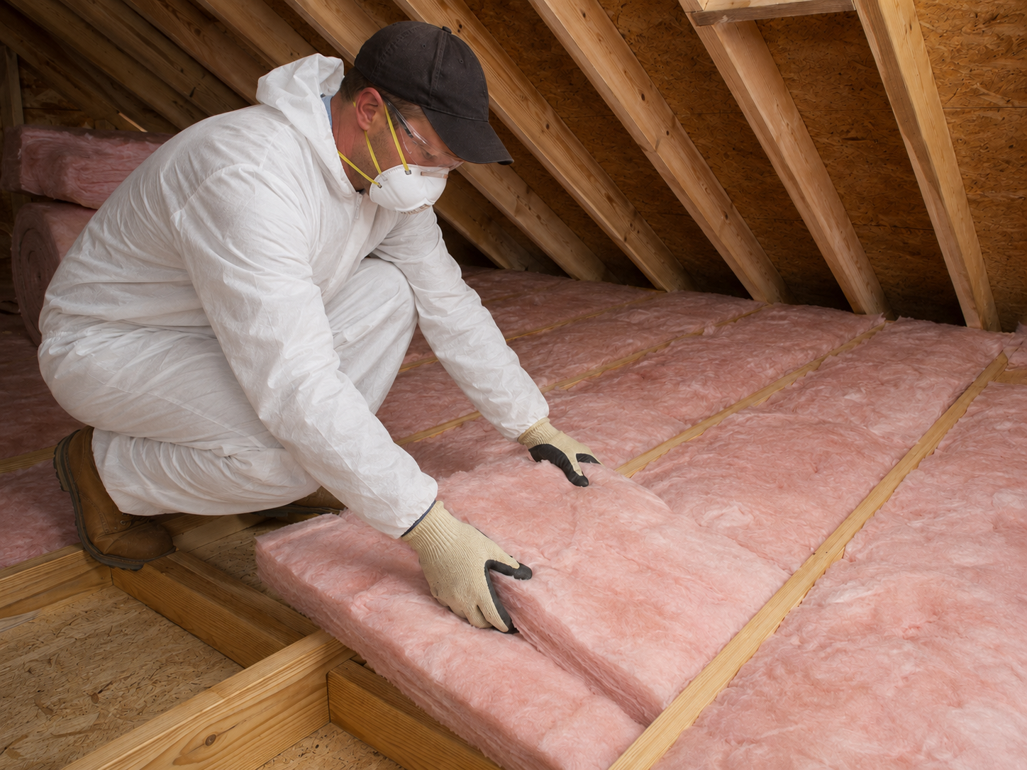 Technician wearing protective equipment while installing fiberglass batt insulation between attic floor joists in an Odenton, Maryland home