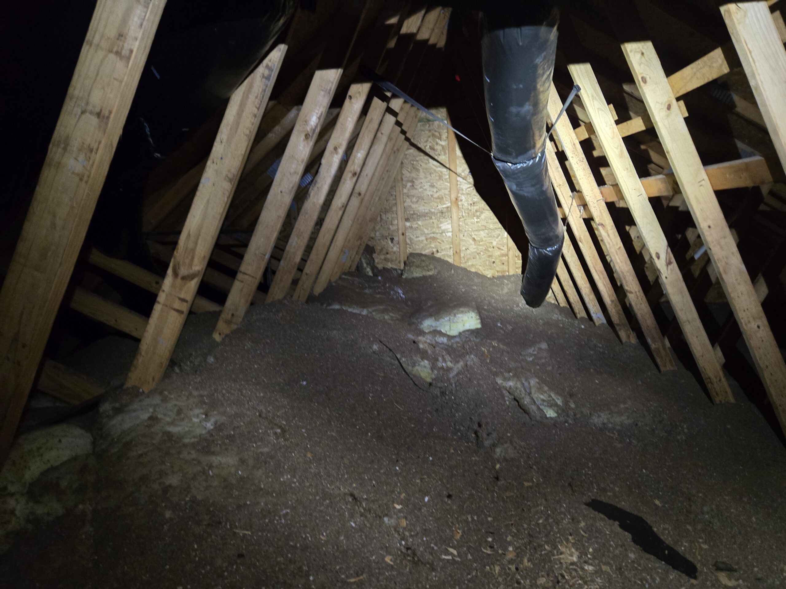 Old loose-fill attic insulation with uneven coverage and exposed fiberglass in an Ellicott City, Maryland home
