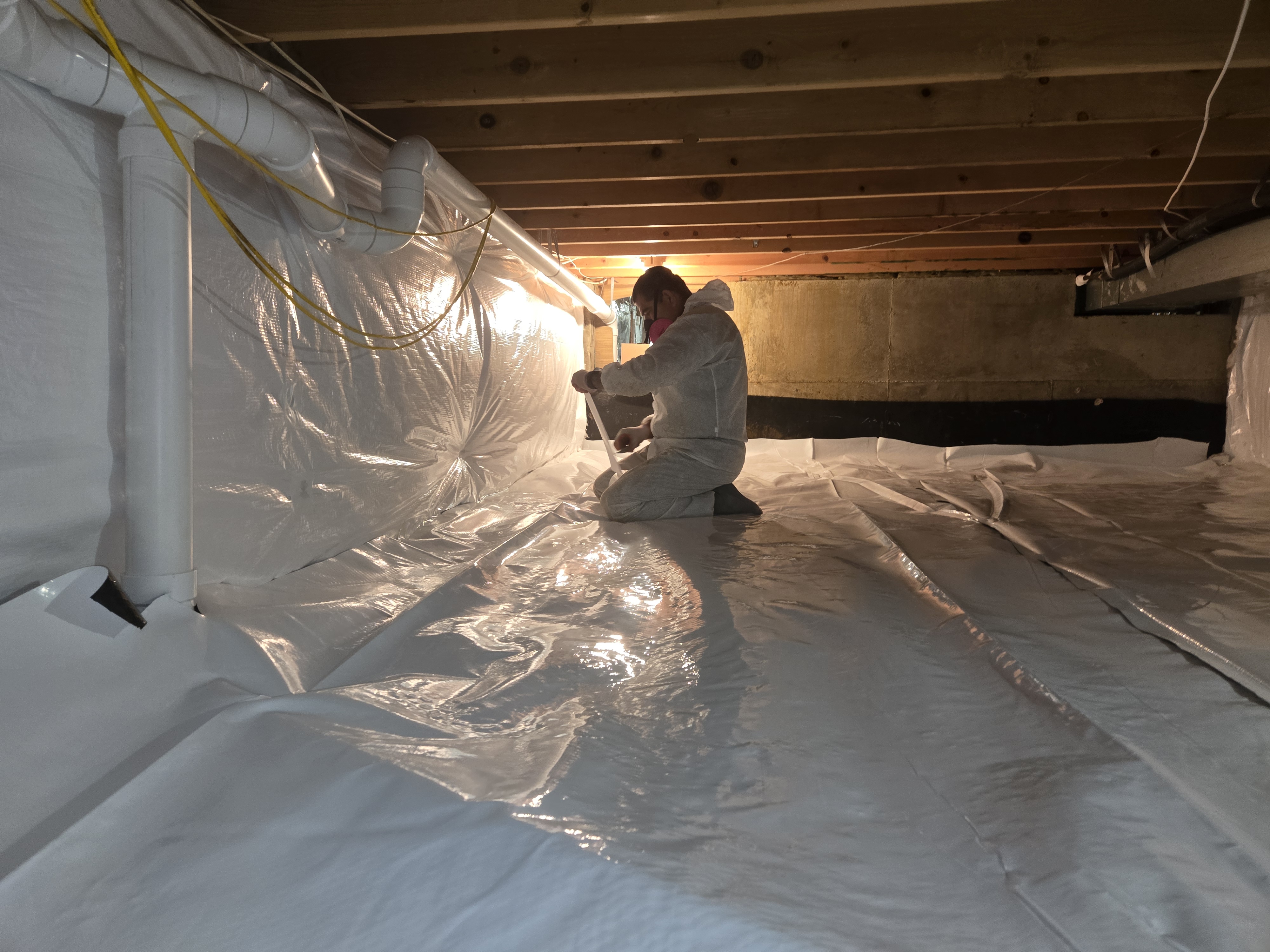 Insulation Contractor in Baltimore City, MD Xanvria technician taping the seams of a reinforced crawl space encapsulation liner in Maryland